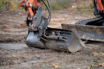 Bucket of a mini excavator during earthworks on a construction site. Concept of construction, mechanized labor, and use of specialized machinery.