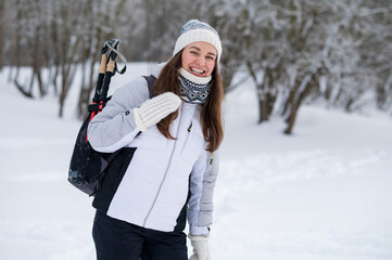 Smiling woman with backpack and nordic walking poles in winter park