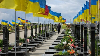 Mourning man go among countless graves of ukrainian soldiers with national flags at military cemetery in Kharkiv. Scene reflects personal sorrow and nation collective loss caused by russian aggression