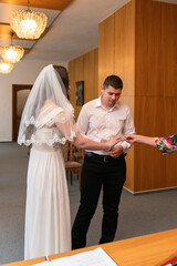 Fototapeta premium Couple exchanges wedding rings in a simple ceremony at a local venue with wooden walls and decorative chandeliers