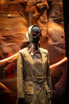 Milan, Italy - 2026, 13 Jan: Gucci FW25 display featuring a chic mannequin in a patterned coat, silk scarf, and sunglasses against an artistic sandstone backdrop