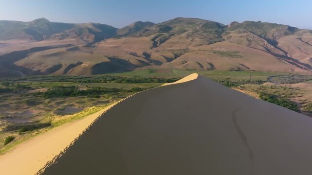 Aerial drone footage captures the majestic Sarykum Dune, the largest sand dune in Europe, located within the protected Dagestan Nature Reserve in the Caucasus Mountains, Russia. The golden sand contra