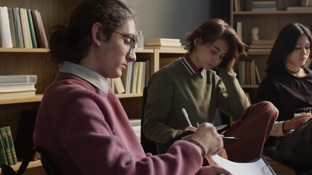 Tilt up shot of teenage boy with glasses focused on filling out psychological evaluation test on clipboard while self assessing mental health in group session in therapists office