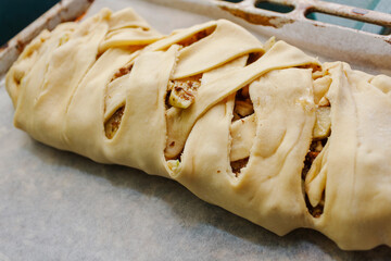 Raw braided apple strudel or pie on baking paper ready for oven. Unbaked homemade sweet pastry.