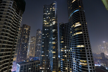 Obraz premium Dense urban skyline at night with illuminated high-rise buildings emerging through atmospheric haze, representing modern metropolitan city life in India
