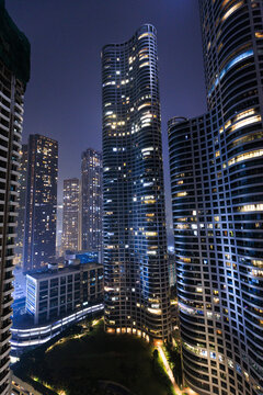 Dense urban skyline at night with illuminated high-rise buildings emerging through atmospheric haze, representing modern metropolitan city life in India