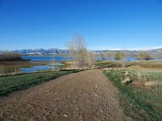 Curving Gravel Path Through Lakeside Meadow with Snowy Mountain Foothills in Spring