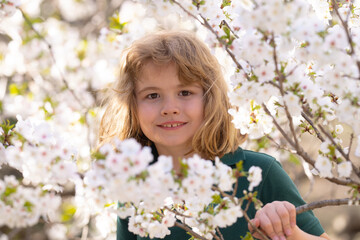 Fototapeta premium The kid smelling spring flowers in blossoms park. Kids face in blossom branches. Pretty child boy 10 year old with flowers over spring blooming nature background close up. Spring season. Childhood.