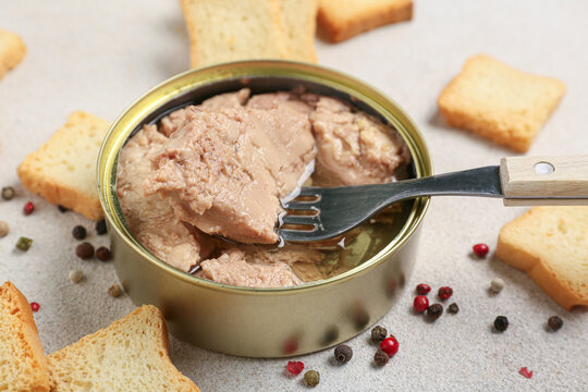 Tin can with tasty cod liver, crackers and peppercorns on light background, closeup