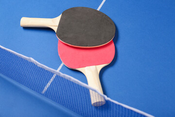 Different ping pong rackets near net on blue table