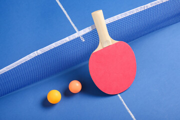 Ping pong racket and balls near net on blue table