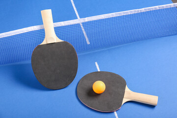 Ping pong rackets and ball near net on blue table