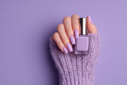 A hand with long purple nails grips a nail polish bottle
