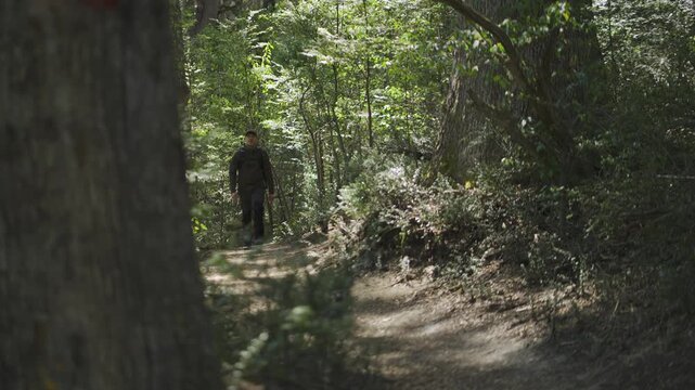 Male traveler with a backpack walking along a shaded dirt trail through a dense evergreen forest towards the camera in Patagonia