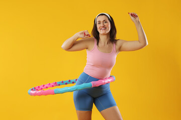 Happy woman training with hula hoop on yellow background