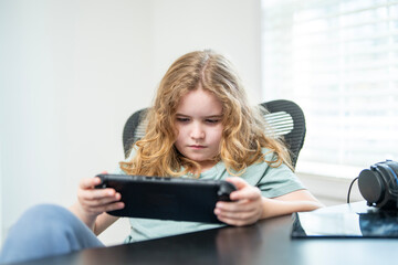 Boy using a gaming device for online game. Child gamer playing a game for streaming. Kid playing a video game in home room. Child playing a game on a mobile gadget.