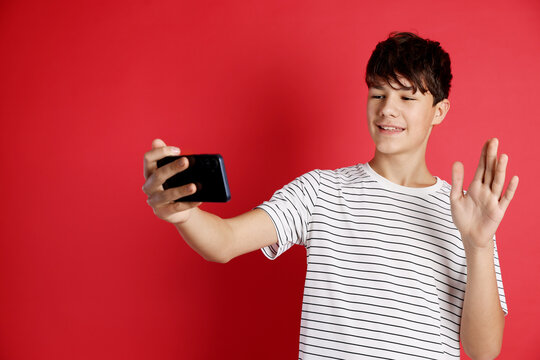 Teenage boy having video chat via smartphone against red background - Powered by Adobe