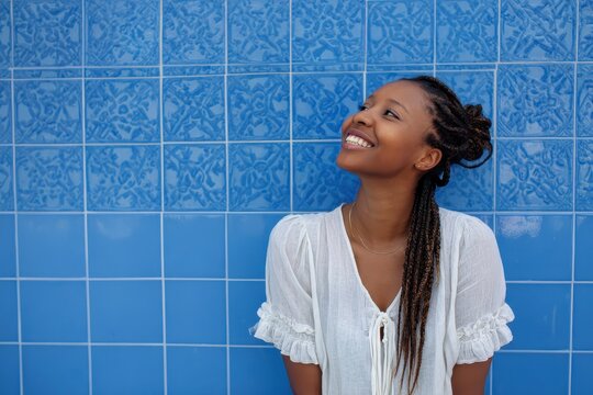 Joyful middle aged woman with braided hair by a blue tile wall
