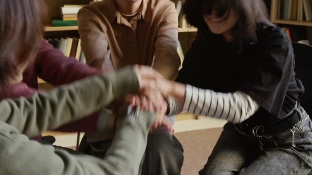 Cropped shot of cheerful teenagers and female therapist throwing up stacked hands sharing mutual support in group therapy session