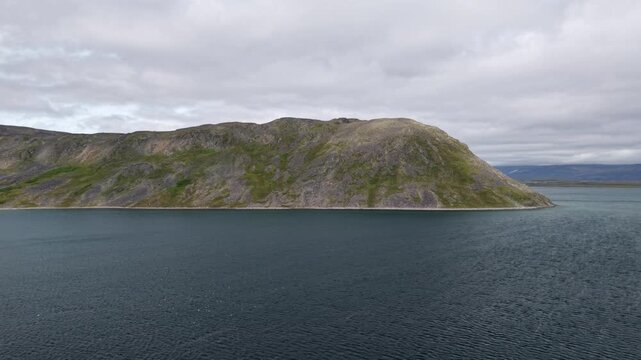 Aerial view of a bold rocky ridge rising from deep blue water in Russia, Chukotka, Lavrentiya Bay at daytime with soft cloud. Strong geology and clean coastline add premium travel value