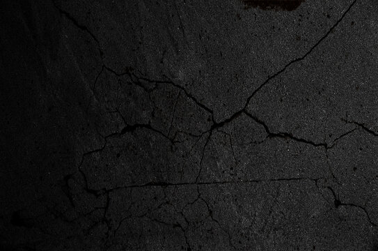 Primer plano de asfalto o concreto oscuro con grietas irregulares que forman una superficie fracturada y texturizada.deterioro urbano y estr&eacute;s geol&oacute;gico.