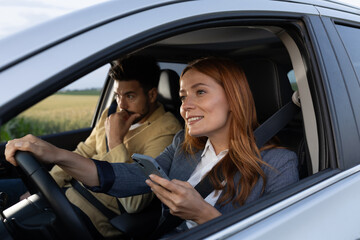 Man sitting in passenger seat concerned while woman driving holds phone in one hand