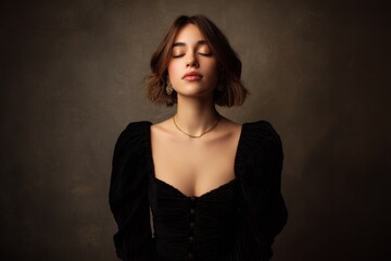 Fototapeta premium A young woman in a black dress poses confidently with her eyes shut in a studio