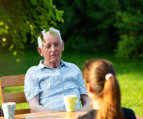 Elderly male sitting across granddaughter outdoors