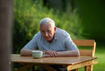 Old man looking at camera while hunched over a teble outdoors