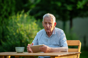Pensioner looking at camera with tablet in hand outside