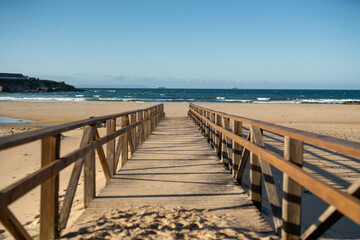 Wooden boardwalk leading to sandy beach and calm ocean under clear blue sky minimal coastal landscape perspective travel nature background