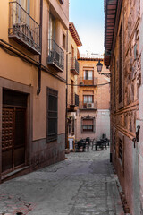 Fototapeta premium Narrow Spanish cobbled street Plaza de Montalbanes (translation: Montalbanes Square) with old residential houses, traditional balconies, window bars and restaurant tables, Toledo, Spain.