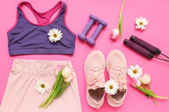 Sportswear with spring flowers and equipment on pink background