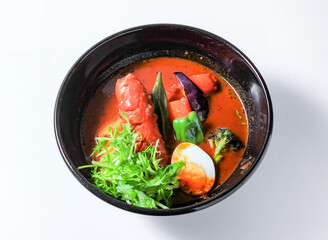 Delicious bowl of spicy red frank curry in bowl with fresh herbs and vegetables isolated on white...