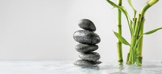 Stack of spa stones and bamboo in water on light background with space for text