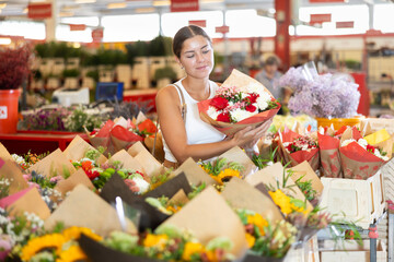 Happy young girl buyer holding bouquet of flowers in large plants market