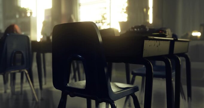 Sunlight streams through the windows of a quiet classroom, illuminating rows of black chairs at wooden desks. The peaceful atmosphere suggests a break in the school day.