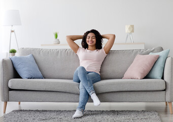 Obraz premium Enjoy freedom, weekend and spare time at home. Happy millennial pretty african american woman rest in silence and cleanliness of new apartment after moving, in living room interior, empty space