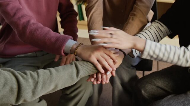 Close up on hands of teenagers and female therapist stacking palms sharing mutual encouragement during group support meeting in therapy room