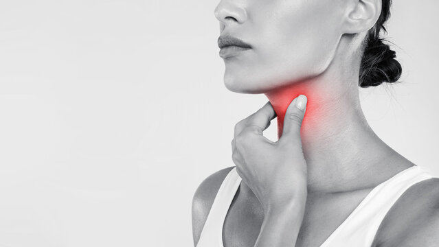 Closeup of sick woman having sore throat, touching her neck with red inflamed zone, suffering from laryngeal disorder, tonsillitis, throat cancer, cold, free copy space over gray studio background
