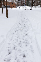 Pedestrian pathway covered with snow through residential park in winter season. Footprints on snow
