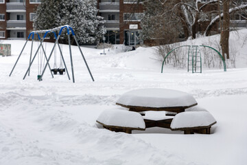 Snow-covered picnic table in a residential park with playground during winter.
