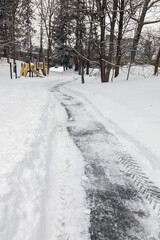 Road in the park covered with salt and melting snow during winter.