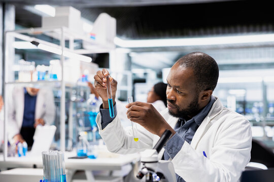 Clinical lab technician analyzes blue liquid chemical sample properties in glass test tube. Research facility employee holds vial containing new compound for medical RD study