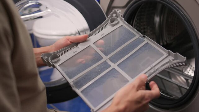 Technician examining dryer lint screen thoroughly, Detailed scene of maintenance technician carefully assessing lint filter inside frontload dryer in laundry room setting