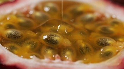 Extreme closeup macro shot capturing the vibrant yellow pulp and dark seeds of a freshly cut passion fruit as a glistening stream of golden liquid slowly pours over the juicy tropical fruit emphasizi.