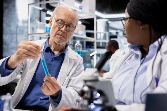 Senior lab manager helped by assistant to do coloring additives test tube sample safety inspection in lab. Laboratory team leader teaching intern to verify chemical safety compliance for products - Powered by Adobe