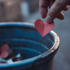 hand dropping red paper heart into blue trash bin