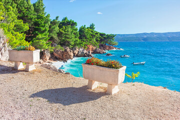 Fototapeta premium Wonderful beach of Croatia. Coastal tranquility. Serene view of Mediterranean Sea, framed by greenery and charming flower boxes. Picturesque coastal landscape with small boats on azure water