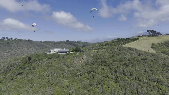 Drone flies left as paragliders fill the sky on a sunny day on the Garden Route in Wilderness, South Africa